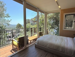Una camera da letto con un grande letto, un balcone con tavolo e sedie in legno e vista sulla città.