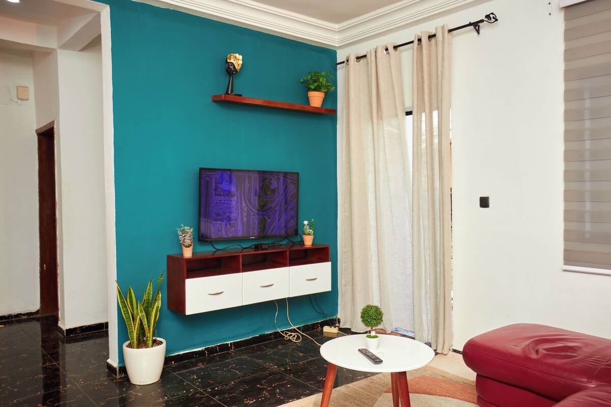 A living room with a teal accent wall, a flat-screen TV, a red sofa, and a small white table.