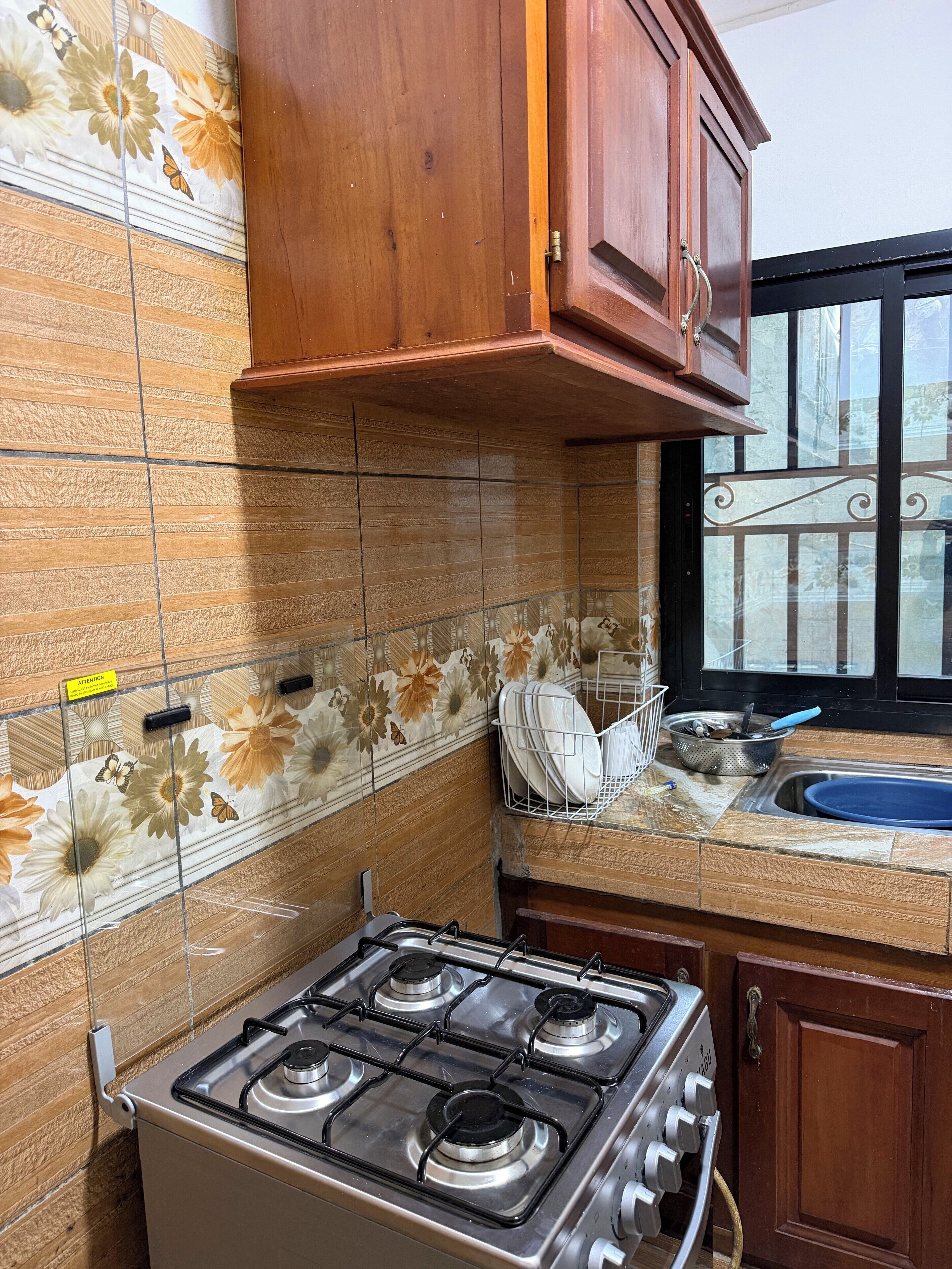 A kitchen with a gas stove, wooden cabinets, a tiled backsplash, and a window with decorative ironwork.