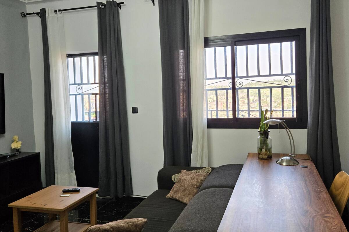 A room with a sofa, a wooden table, a TV, and a window with curtains.