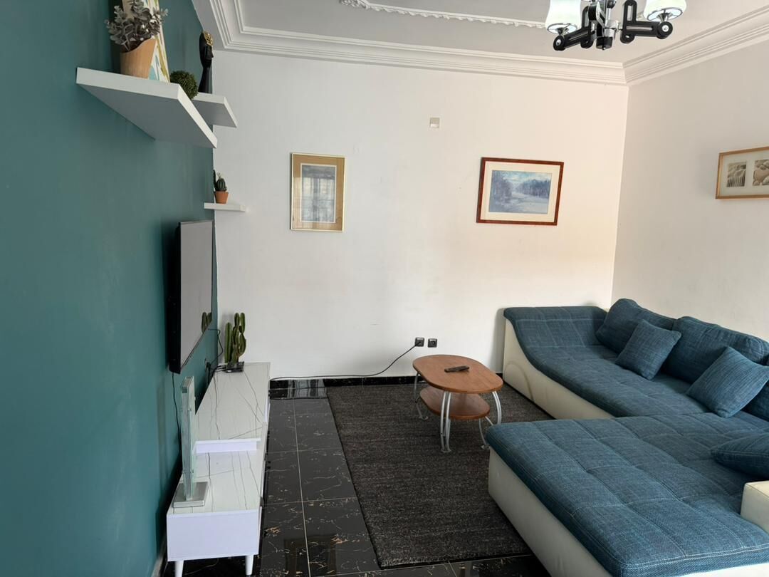 En stue med en blå sofa, et rundt bord og et hvidt skab.