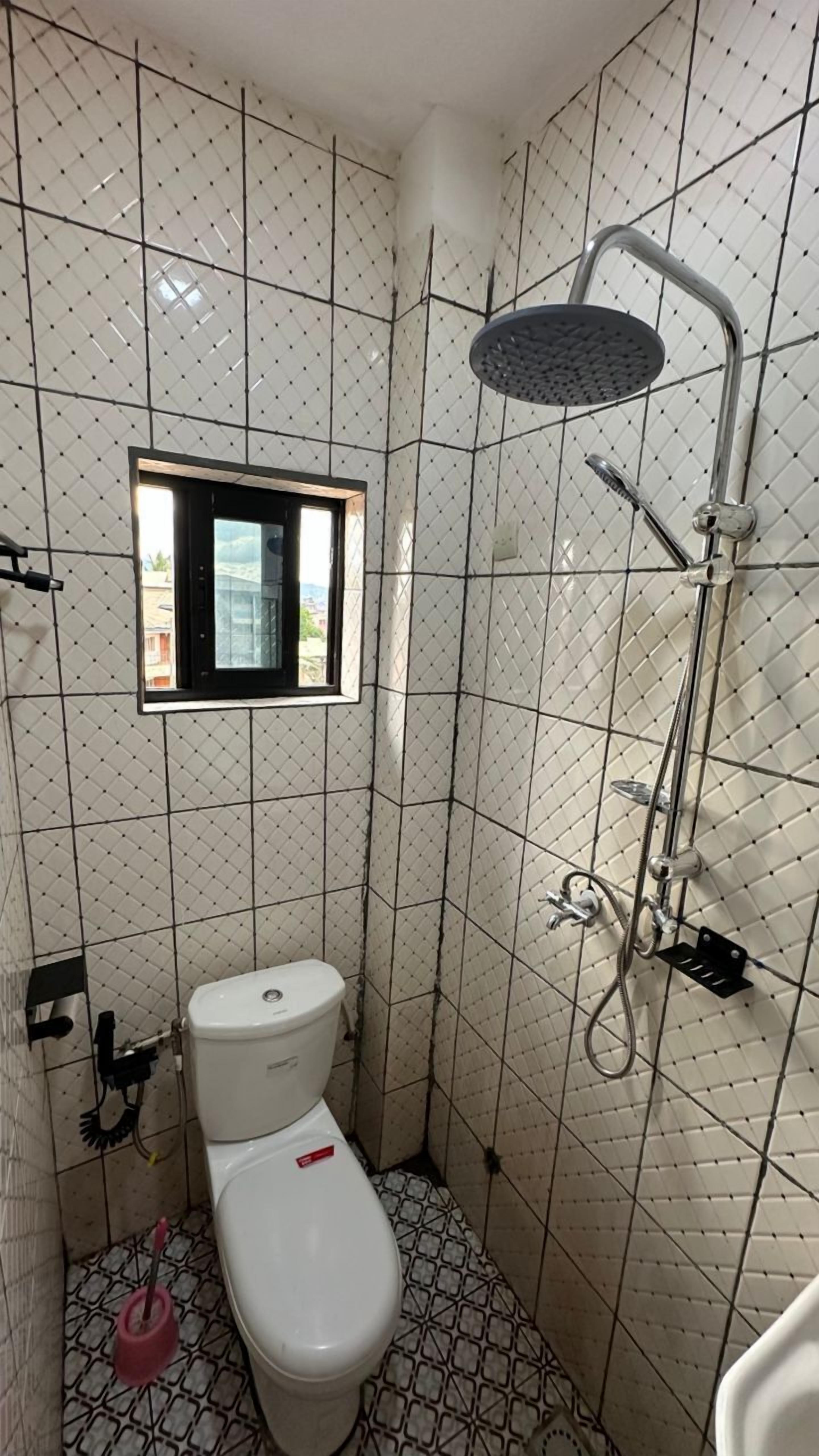 A small, tiled bathroom with a toilet, a window, and a shower.
