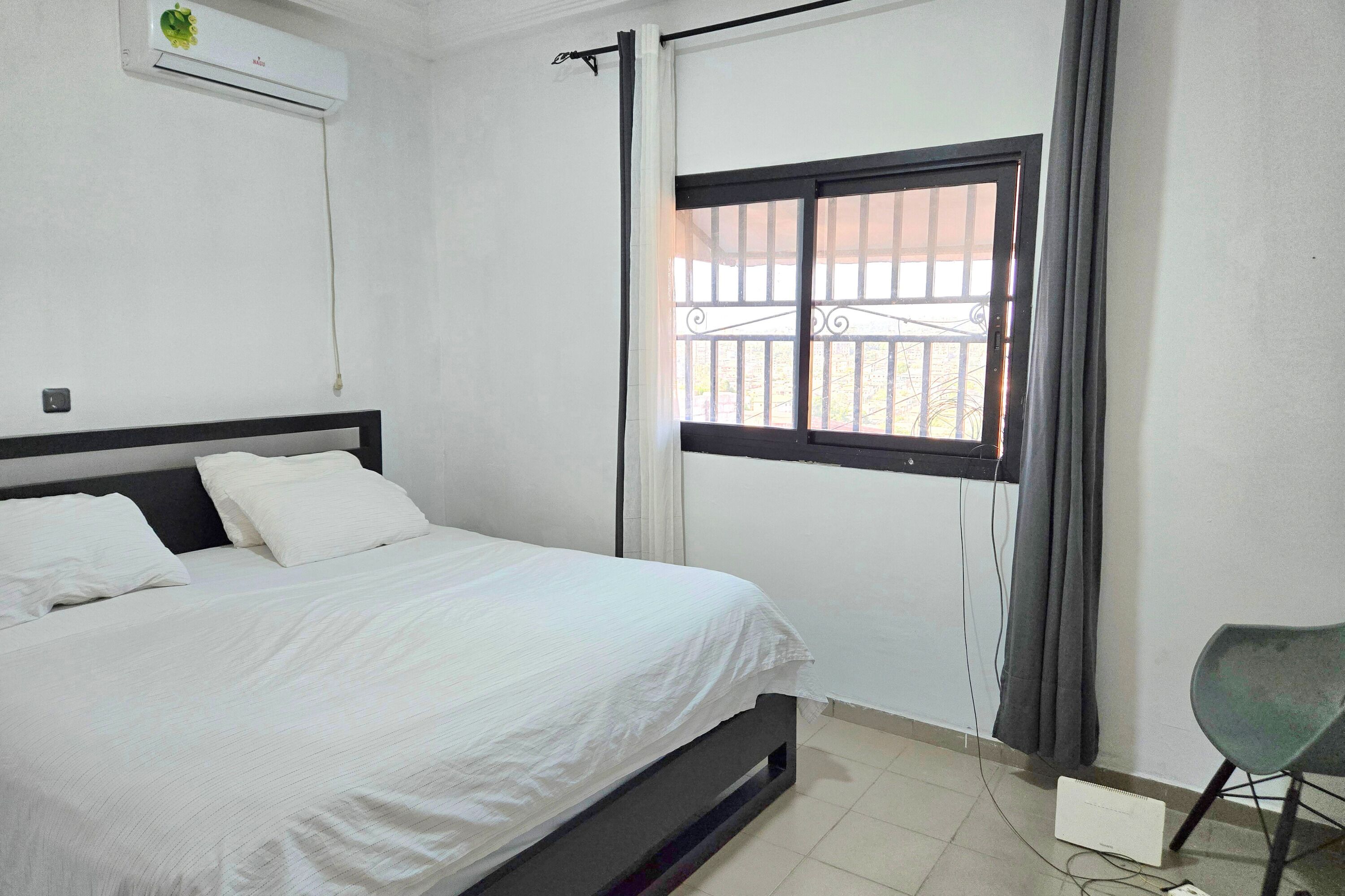 Een slaapkamer met een bed, een raam met uitzicht, een airconditioning en een stoel.