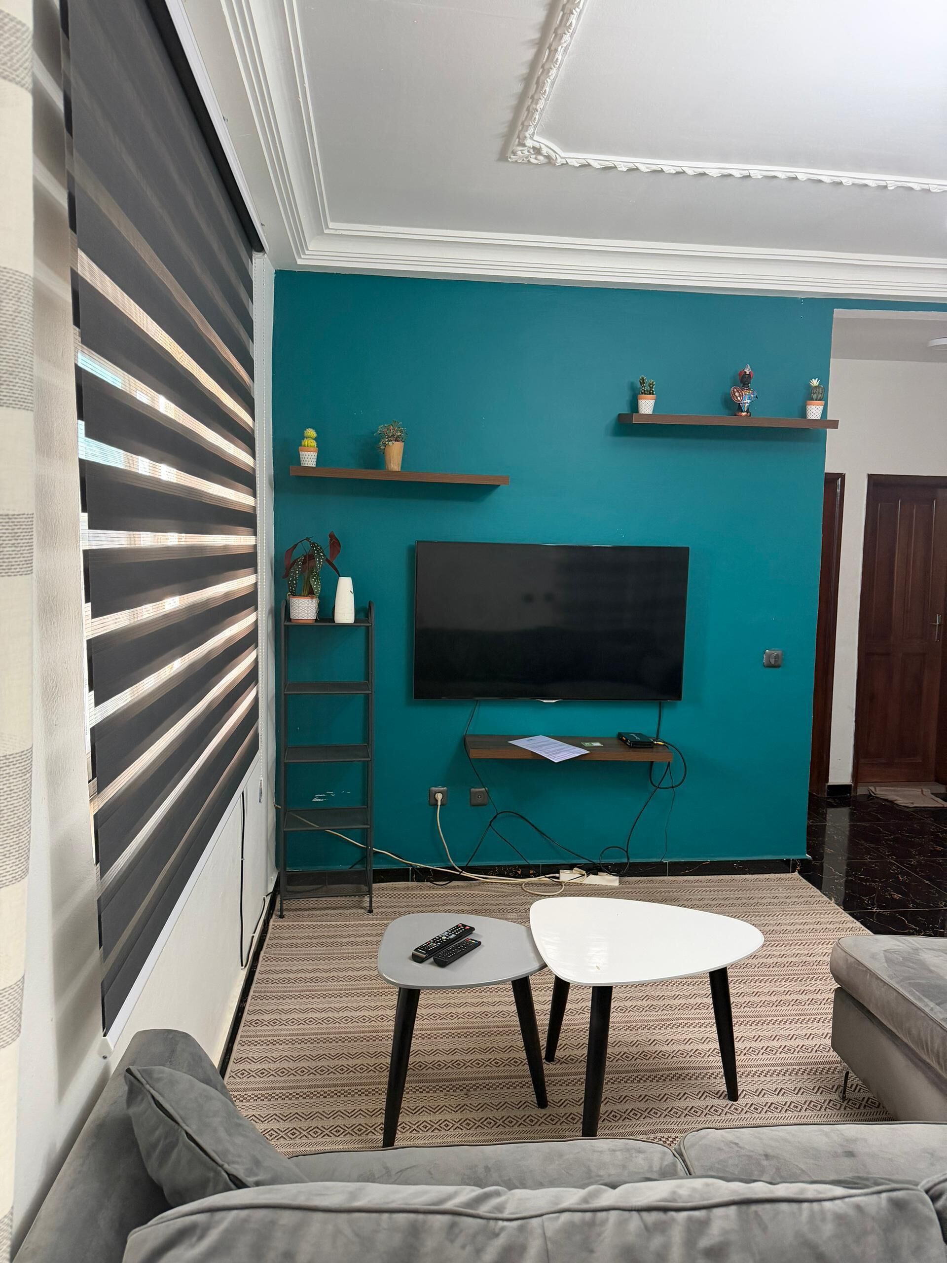 Un salon avec un mur de couleur turquoise, un téléviseur à écran plat, un canapé, une table basse et un meuble pour la télévision.