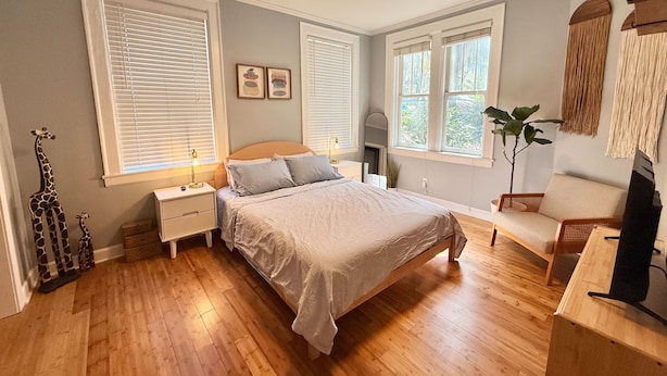 Quarto com cama, mesas de cabeceira, ventilador de teto e janelas amplas.