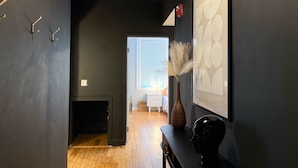 Um corredor com piso de madeira, parede preta, obra de arte emoldurada, um vaso com plumas de capim-do-avelã e uma decoração de caveira.