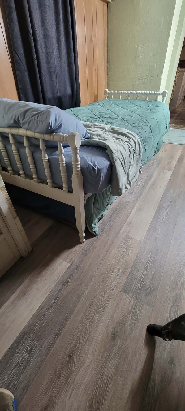 Una habitación con una cama de madera, un colchón verde y piso de madera.