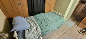 A single bed with a quilted green bedspread and a blue pillow.