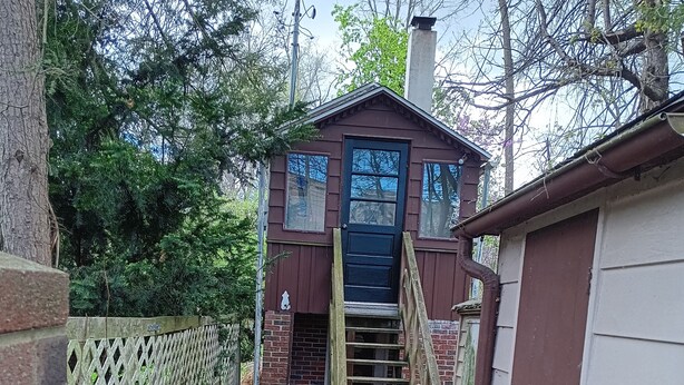 Un étroit sentier mène à un petit bâtiment doté d’une porte et d’un escalier en bois.