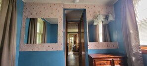 Una habitación con pared azul, cómoda de madera, espejo y ventana con cortinas.