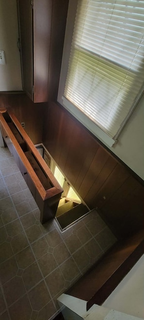 A room with a wooden bench, a window with blinds, and a tiled floor.