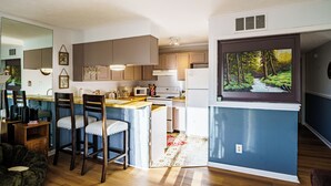 A modern kitchen with wooden cabinets, a central island, and a large window with a forest view. - Sunset Lover - Breathtaking Balcony Views, Sleeps 4, 15 Minutes Walk to Downtown (Gatlinburg)