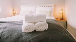Een keurig opgemaakt bed met witte lakens en een groene plaid.