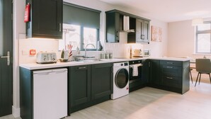 Een moderne keuken met donkere kastjes, een vaatwasser, een wasmachine en een aanrecht met een broodrooster en bestek.