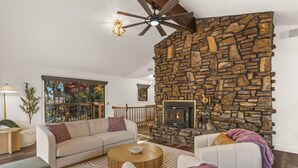 A living room with a stone fireplace, a sofa, a coffee table, and a ceiling fan. - Dragonfly Landing on Beaver Lake, w/ hot tub (Rogers)