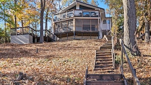 A modern two-story building with a balcony, surrounded by trees and a wooden staircase. - Dragonfly Landing on Beaver Lake, w/ hot tub (Rogers)
