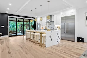 A modern kitchen with a central island, bar stools, stainless steel appliances, and a large refrigerator. - Buckhead Modern Tropical Estate (Atlanta)