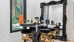 Eine Bar mit einem Glastisch, einem schwarzen, verzierten Spiegel und goldenen Barhocker.