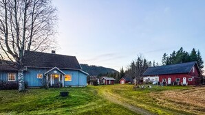 Maalaismaisema, jossa on sininen talo, punainen lato ja sorainen polku.