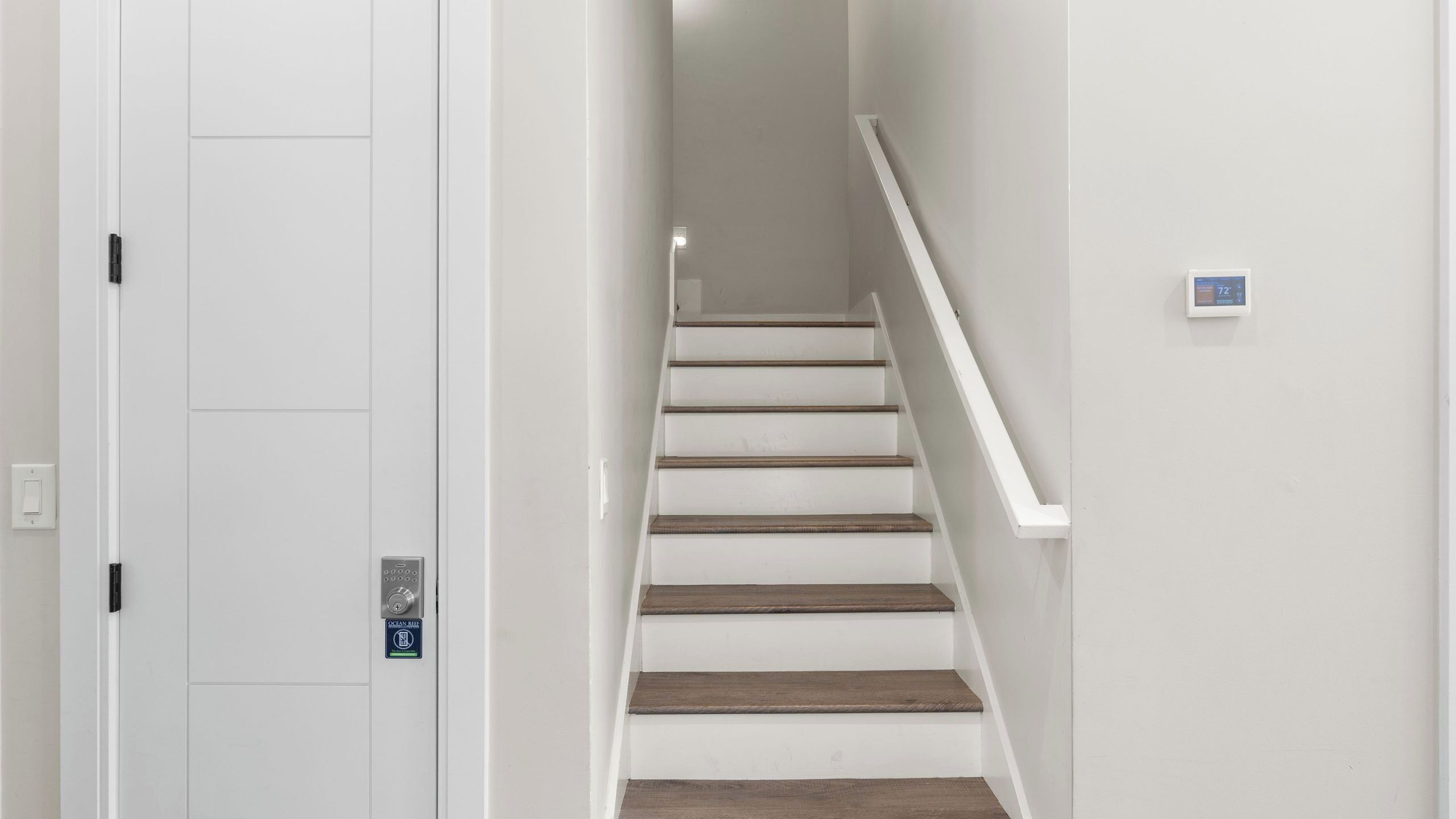 A staircase with wooden steps and white walls, leading to a door with a security keypad.