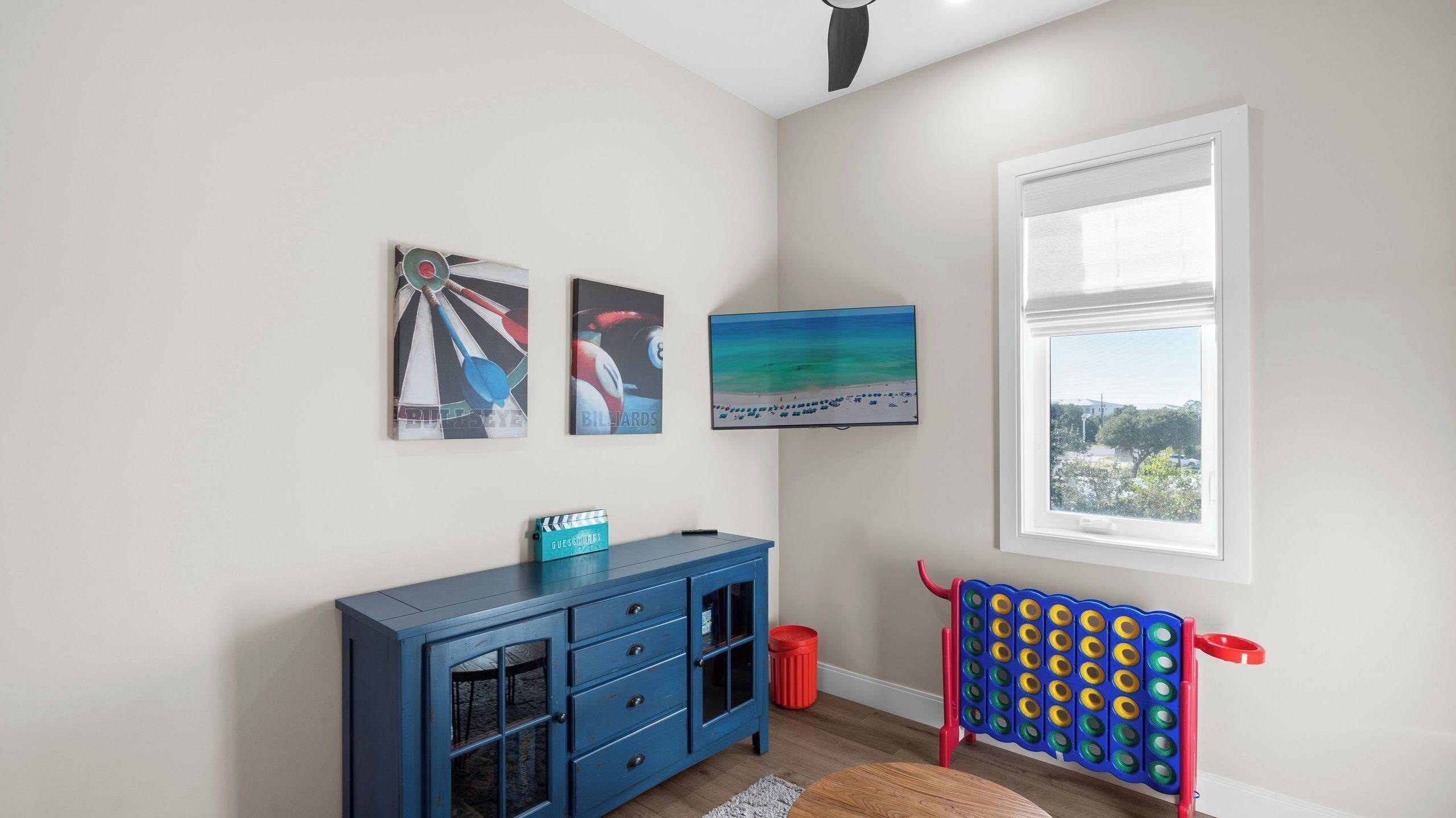 A room with a blue cabinet, a television, a window with a view, and two wall art pieces.