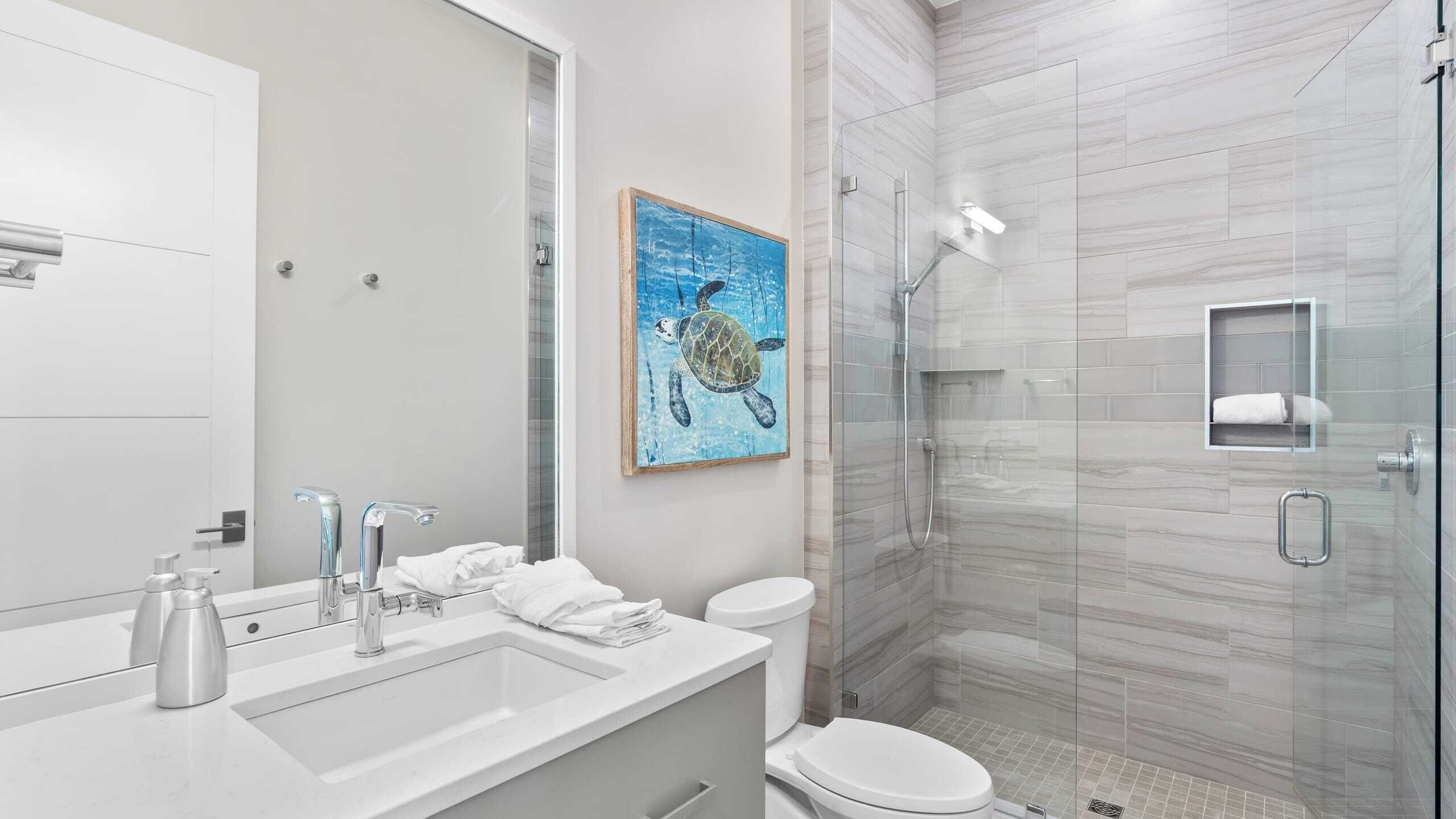 A modern bathroom with a glass shower enclosure, a white sink with two faucets, and a toilet.