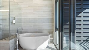 Een moderne badkamer met een vrijstaand bad, een douchecabine met glazen wanden en uitzicht op een houten terras door grote ramen.