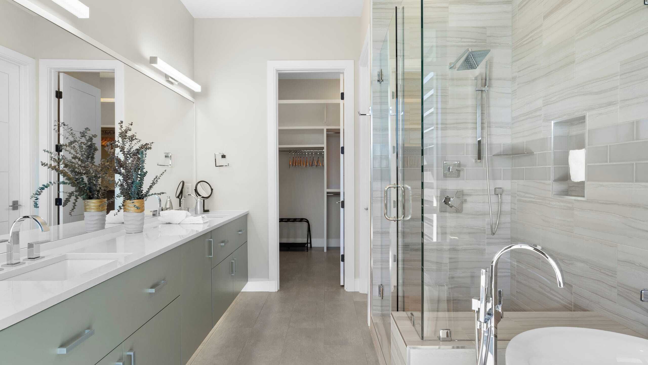 A modern bathroom with a glass-enclosed shower, a large vanity with a mirror, and a walk-in closet.