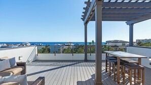 A rooftop terrace with a pergola, outdoor furniture, and a view of the sea. - Rooftop Deck w/ Gulf Views, Game Room Modern 30A by Avantstay (Santa Rosa Beach)