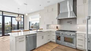 A modern kitchen with stainless steel appliances, light wood cabinetry, and a large window overlooking a scenic view. - Rooftop Deck w/ Gulf Views, Game Room Modern 30A by Avantstay (Santa Rosa Beach)