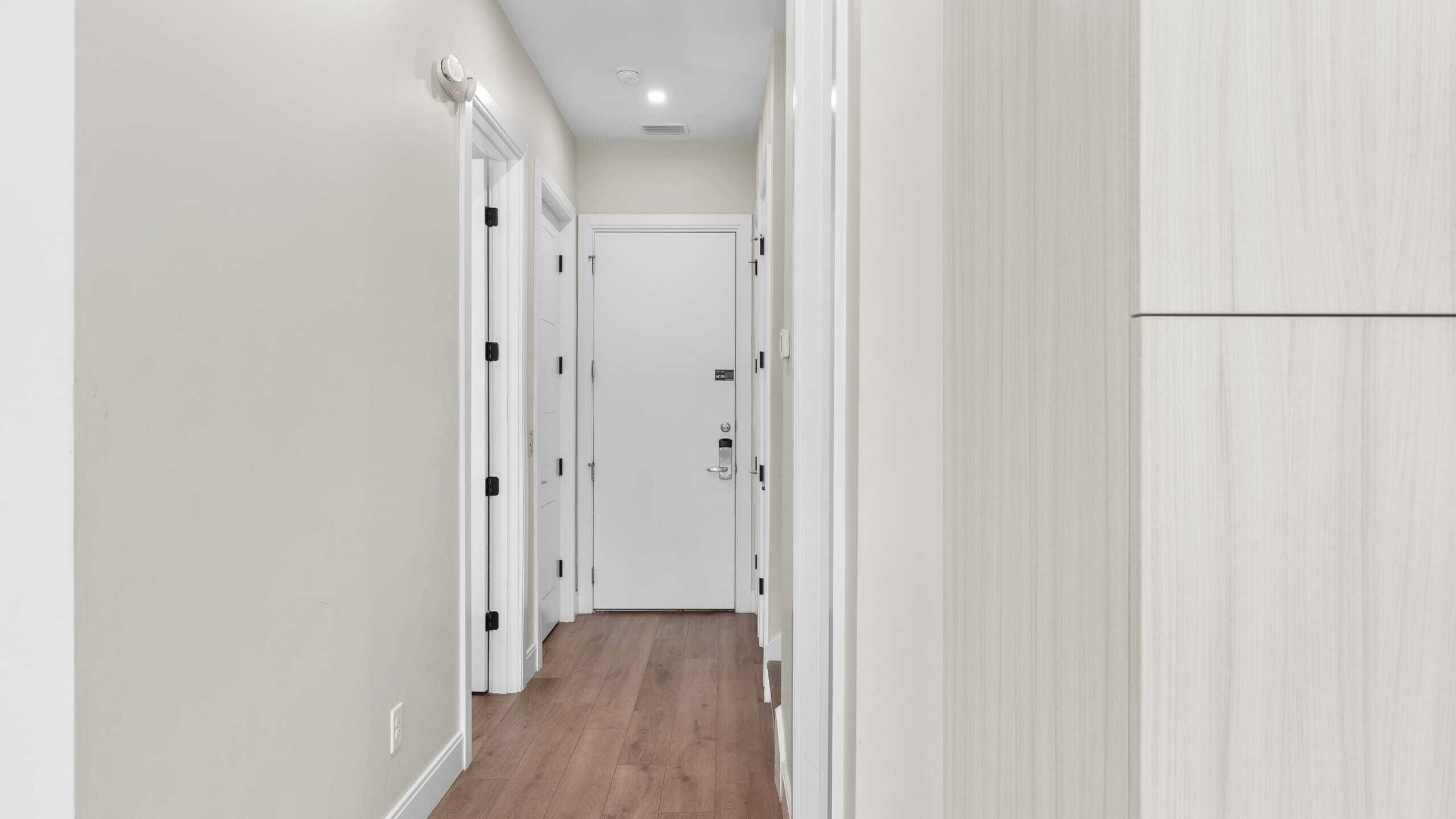 A narrow hallway with white walls, a wooden floor, and white doors with black handles.