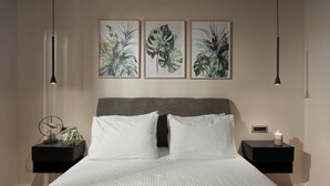 Una camera da letto con un letto, due comodini, una sveglia a parete e stampe botaniche incorniciate.