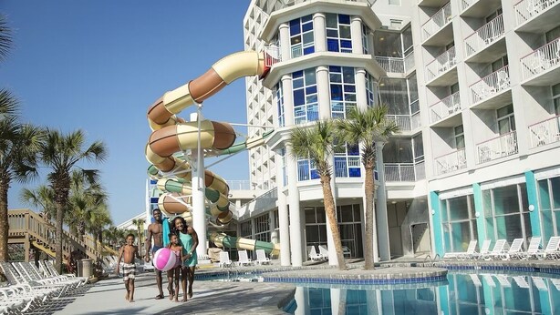 Área de piscina de un resort con tobogán de agua, sillas de descanso y una piscina.