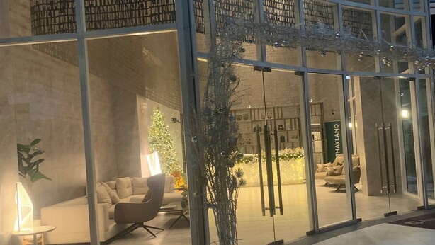En moderne hotellobby med en glasfacade, et siddeområde med sofa og lænestole, samt en potteplante.