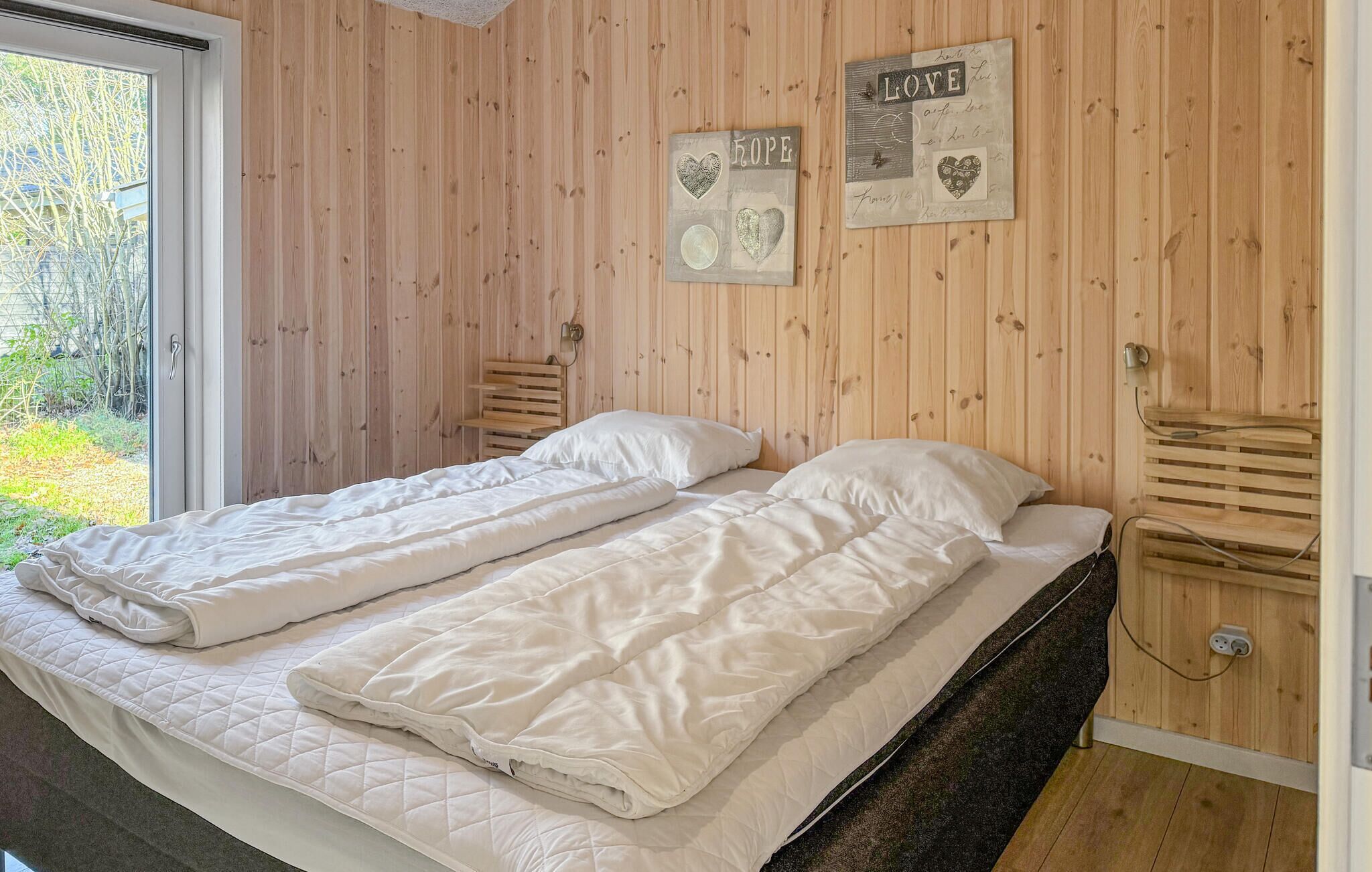 Une pièce avec un mur en bois, un lit recouvert de draps blancs et deux appliques murales.