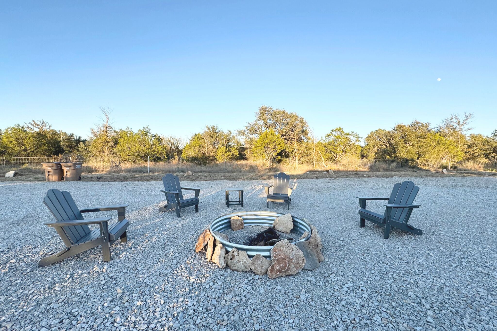 A gravel area with a fire pit and four Adirondack chairs.
