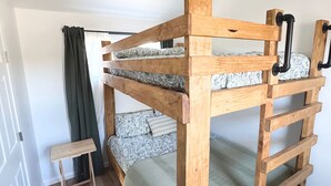 Uma cama beliche com estrutura de madeira e puxadores de metal preto, um banquinho de madeira pequeno e um edredom estampado.