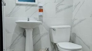 A bathroom with a pedestal sink, toilet, and a trash bin. - Hotel Amanecer Atitlán (San Juan La Laguna)