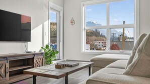 Een moderne woonkamer met een groot raam, een flatscreen televisie, een houten salontafel en een beige bank.