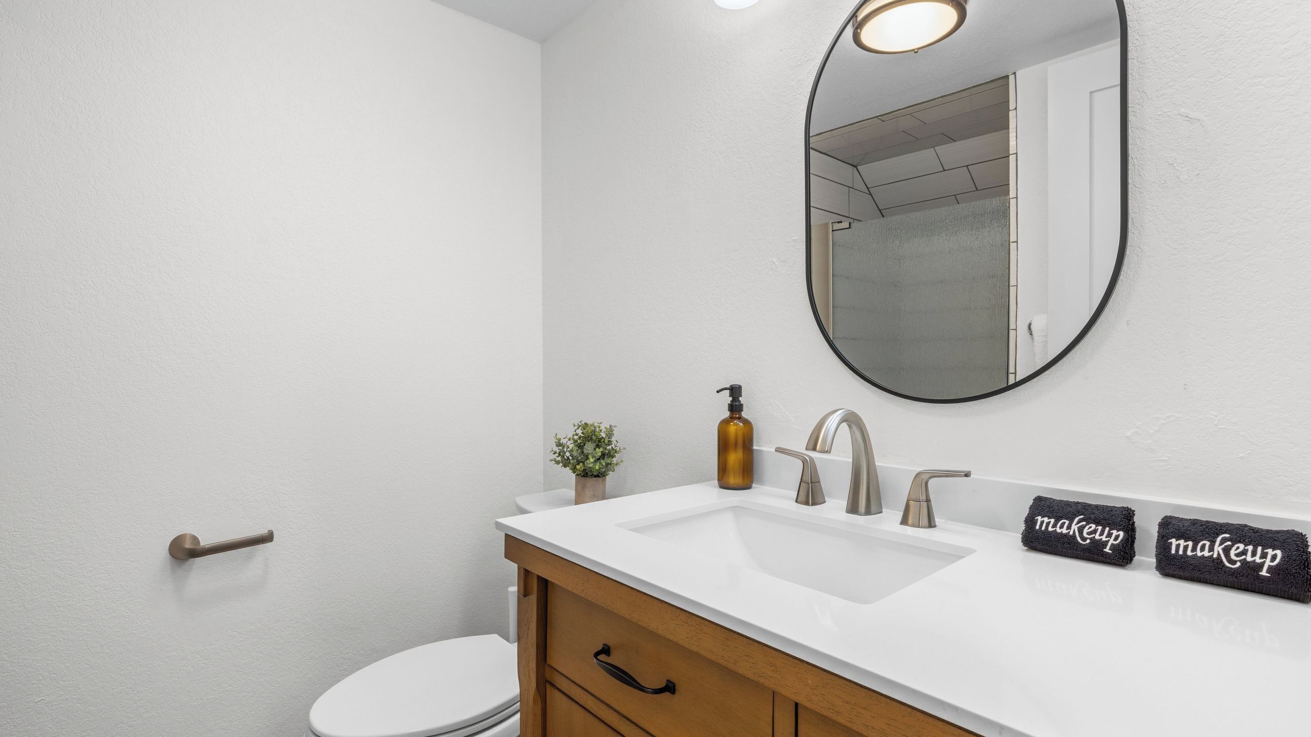 A bathroom with a white sink, a mirror, a toilet, and a wooden cabinet.