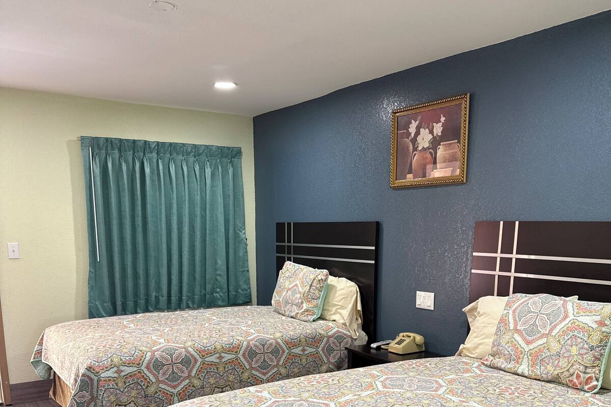 A hotel room with two beds, a nightstand, a telephone, and a painting on the wall.