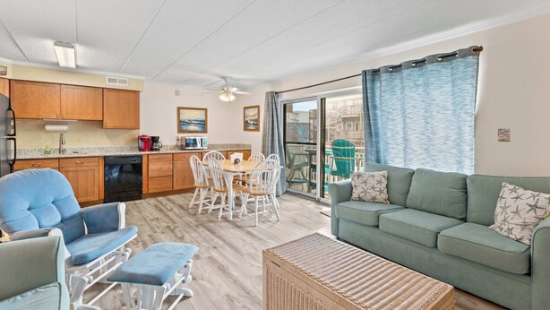A spacious living area with a green sofa, a dining table with chairs, and a kitchen with wooden cabinets and a dishwasher. - Salty Sands 4 208 (Ocean City)