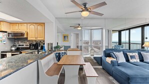 Eine moderne Küche mit Holzausstattung, einer Granitarbeitsplatte und einer eingebauten Mikrowelle. Es gibt einen Essbereich mit Holztisch und Bänken, sowie ein blaues Sofa mit Zierkissen.