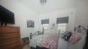 Un dormitorio con cama, cómoda, televisor y ventana con persianas.