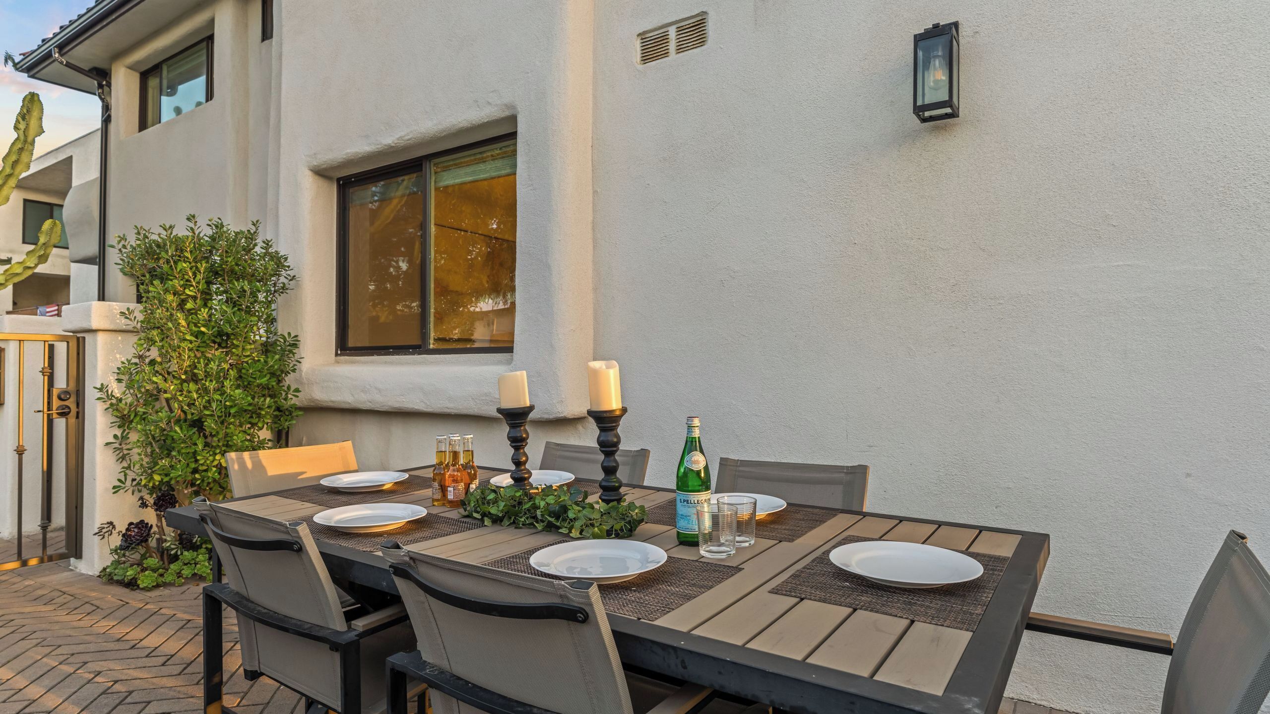 An outdoor dining area with a table set for four, surrounded by chairs, and a potted plant.