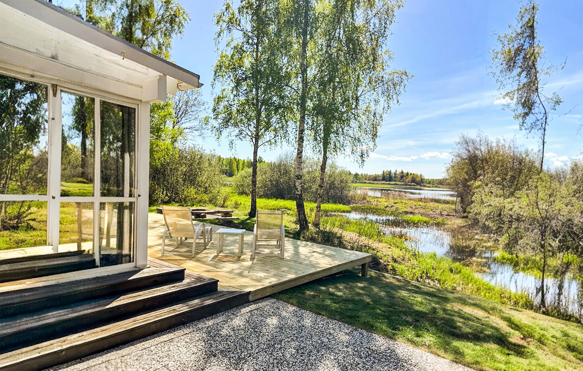 A modern house with a deck overlooking a river, surrounded by trees.