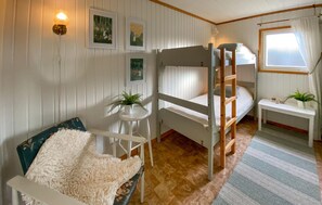 Ett rum med en våningssäng, ett litet bord och krukväxter, vita väggar och ett fönster med gardiner.