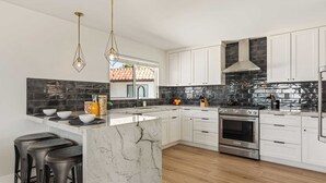 A modern kitchen with white cabinets, a marble island, stainless steel appliances, and a black backsplash. - Rooftop w/ Hot Tub, Ocean Views 259 Trailhead Trestles 1 by Avantstay (San Clemente)