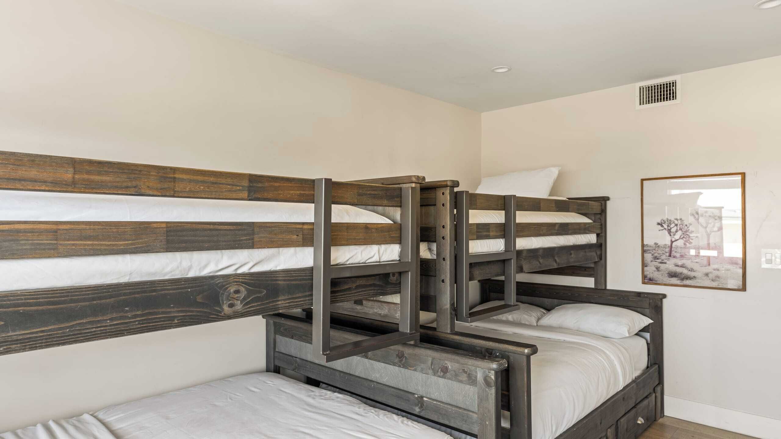 A bunk bed room with wooden headboards and metal frames, white bedding, and a framed picture on the wall.