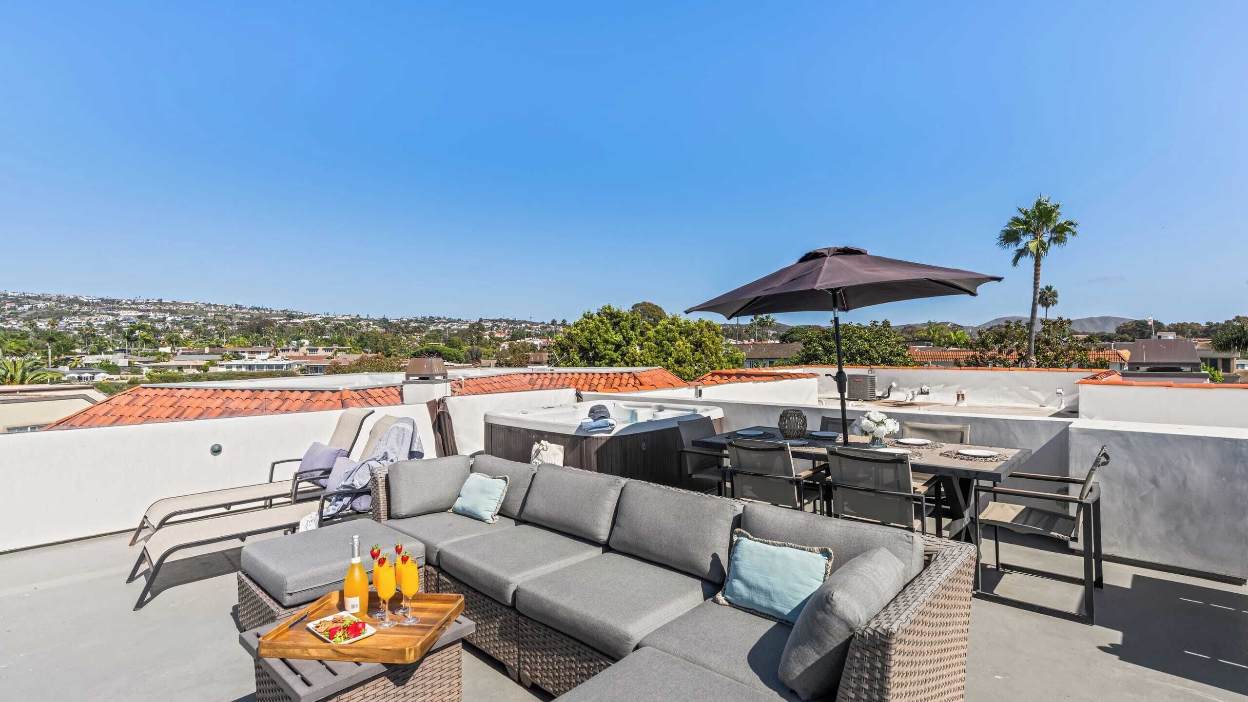 Une terrasse sur le toit avec un canapé gris, une table à manger et des chaises, un barbecue et un grand parasol.